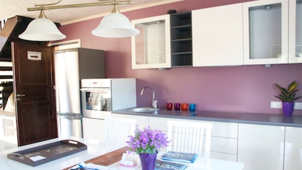 Keittiön takaseinä on trendikkäästi purppura. Linjakkaat tasot tuovat tyyliä kesäkodin keittiöön.