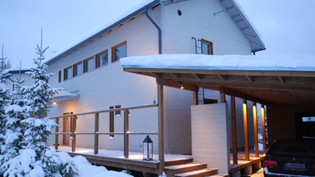 Sisäänkäynnin vieressä on autokatos. Talon julkisivu on pelkistetty mutta näyttävä.