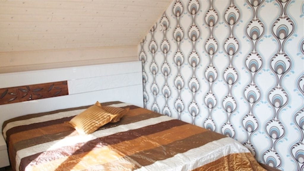 Yksi makuuhuoneen seinistä on tapetoitu nykytrendin mukaisesti kuvioidulla tapetilla. Näyttävä päiväpeitto tuo pieneen huoneeseen särmää. Myös puukuviointi takaseinän paneloinnissa on persoonallinen.