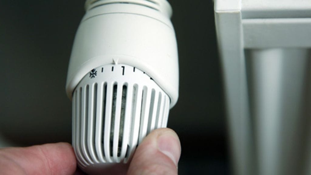 Mies säätää termostaatilla huoneen lämpötilaa.