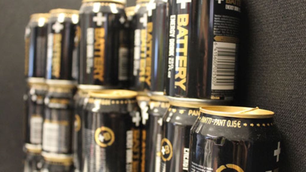 Piian työpöydän ympärille on kerääntynyt komea torni energiajuomatölkkejä