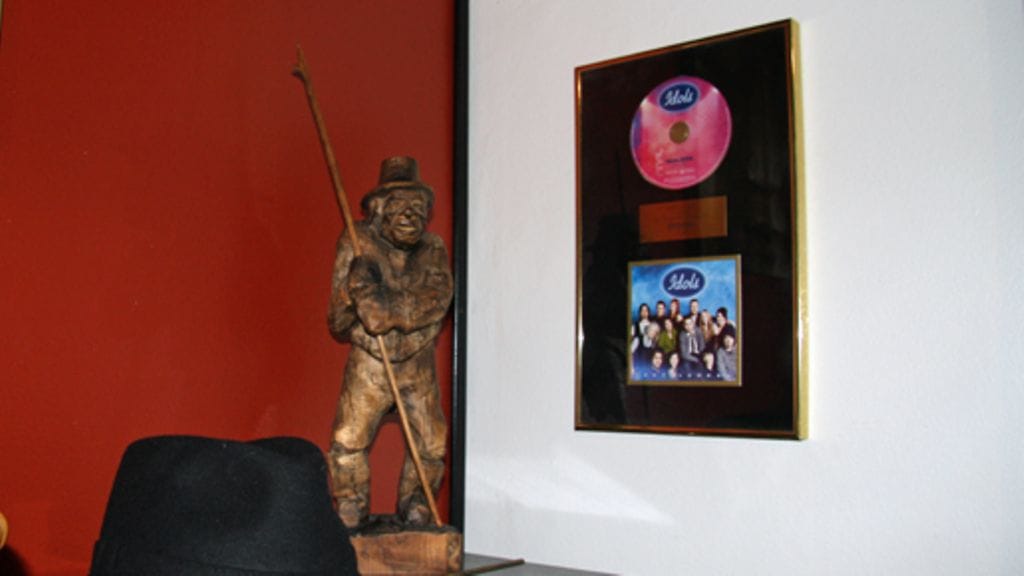 Koopin Idols-kultalevy on ripustettuna pianon taakse. Pianon päällä makaa Koopin tavaramerkki, hattu. Kuva: MTV3.