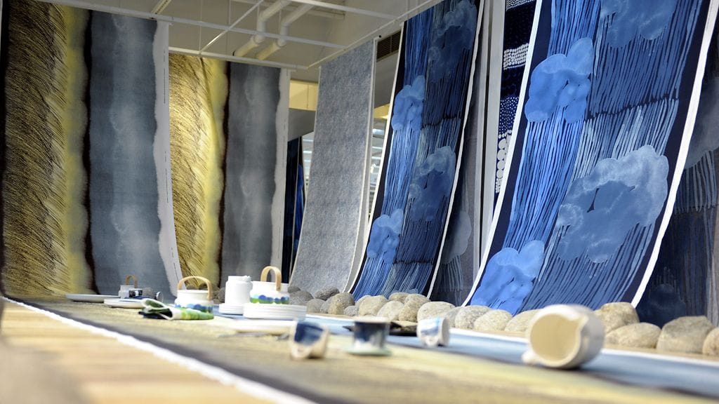 Kuvassa suunnittelija Aino-Maija Metsolan kankaita: Kuuskajaskari (lattialla ja vasemmalla), Harmaja (nurkassa) ja Jussarö (seinällä oikealla).