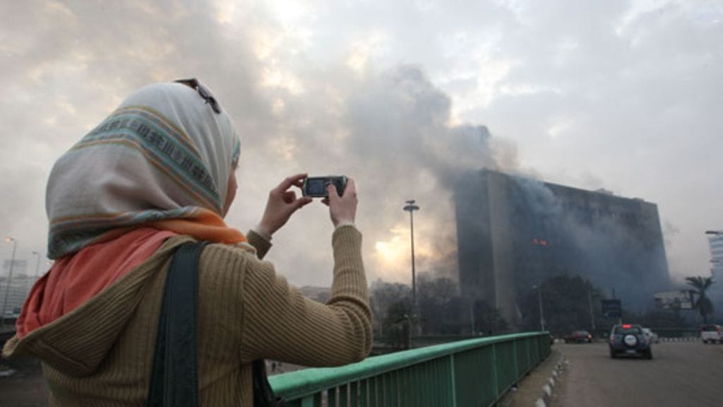 Egyptiläisnainen ottaa kuvaa palavasta NDP-puolueen päämajasta Kairossa 29. tammikuuta 2011. (EPA)