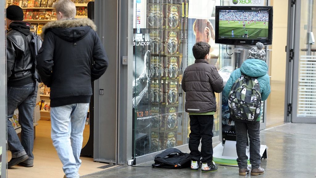 Nuoria koululaisia pelaamassa pelikonsolilla pelikaupan ulkopuolella Kampin kauppakeskuksessa.