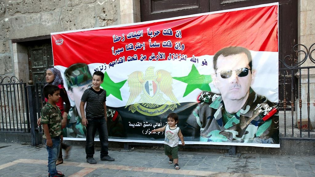 Lapset leikkivät al-Assadia esittävän julisteen edessä kesäkuussa, jolloin mies voitti ylivoimaisesti maassa järjestetyt presidentinvaalit.