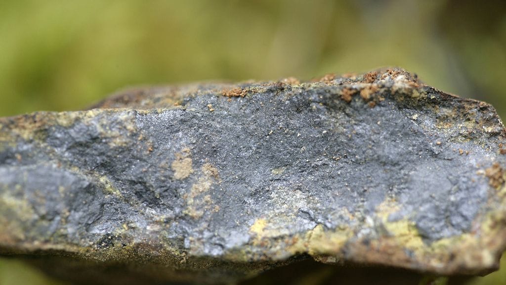 Rumavuoman alueelta vuonna 2008 löydetty näyte, jossa tumma alue on uraania ja ylhäällä pienet keltaiset hiput kultaa.