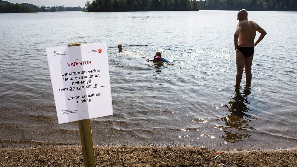 Ihmisiä uimassa ja veden laadun heikentymisestä varoittava kyltti Tohloppijärven rannalla Tampereella tiistaina 29. heinäkuuta 2014.