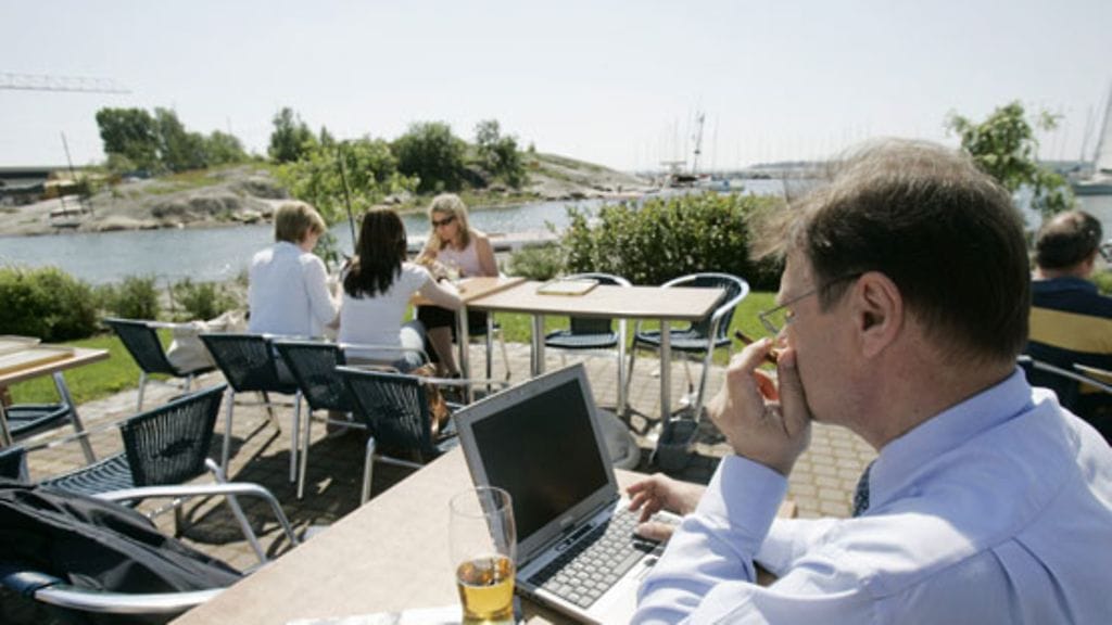 Keski-ikäinen mies polttaa tupakkaa, juo olutta ja käyttää samalla kannettavaa tietokonetta ulkoilmakahvilassa Helsingin Kaivopuistossa. Ilmainen wlan-yhteysverkko ja internet mahdollistavat etätyöskentelyn, ja työnarkomaani paiskii töitä helteelläkin.