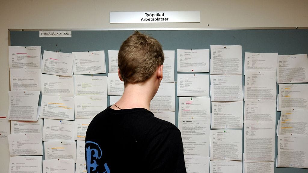 Nuori mies tutkii ilmoitustaulua työnhakukeskuksessa Helsingissä.
