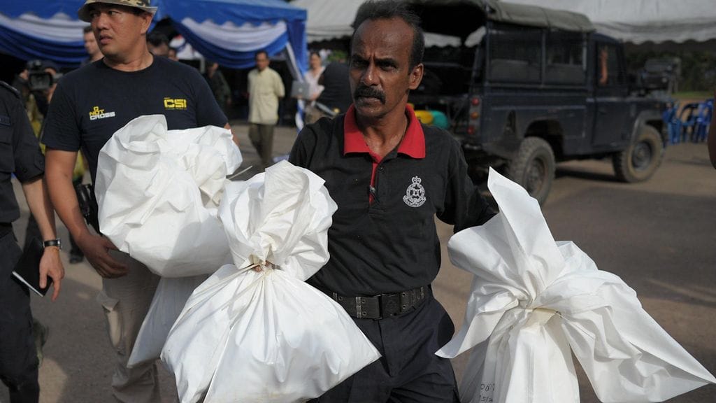 Malesialainen poliisi kantaa muovipusseja, joiden sisällä on ihmisten jäänteitä.