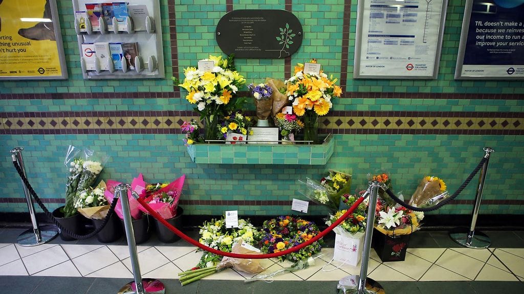 Kukkia Aldgaten metroasemalla Lontoossa. Muistotaulusta näkee aseman iskuissa kuolleiden nimet.