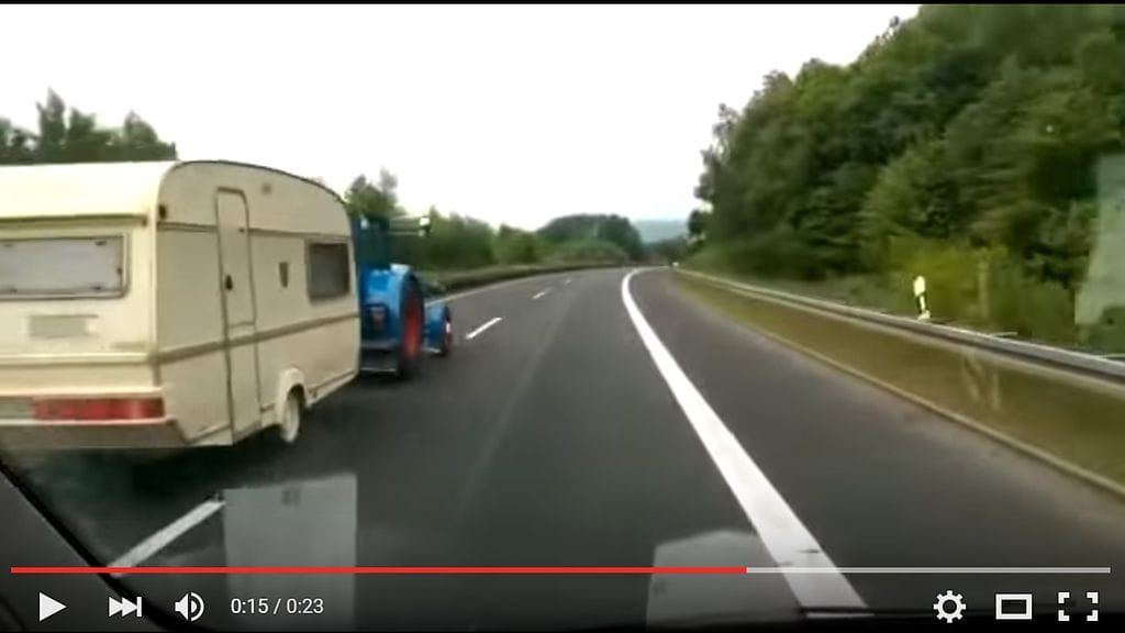 Videolla sininen traktori vetää perässään asuntovaunua.