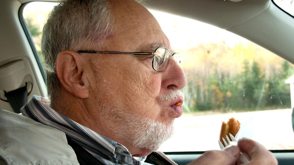 Mies ruokailee autossa.