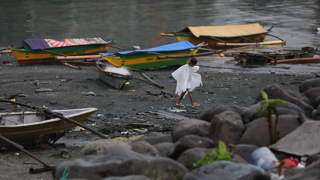 Muoviseen sadetakkiin pukeutunut filippiiniläinen kulkee maihin kiinnitettyjen veneiden ohi.