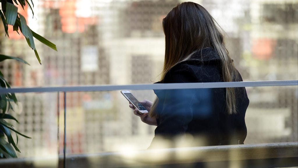 Nuori tyttö käyttää älypuhelinta hengaillessaan kauppakeskuksessa. Kuvituskuva.