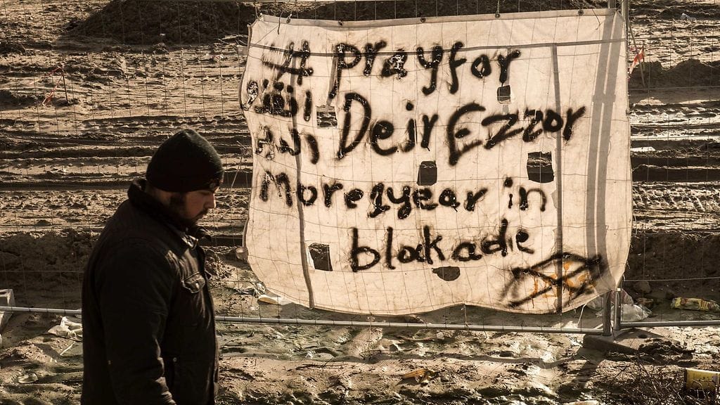 Mies kävelee "Pray for Deir Ezzor" -julisteen ohi pakolaisleirillä joulukuussa 2015.