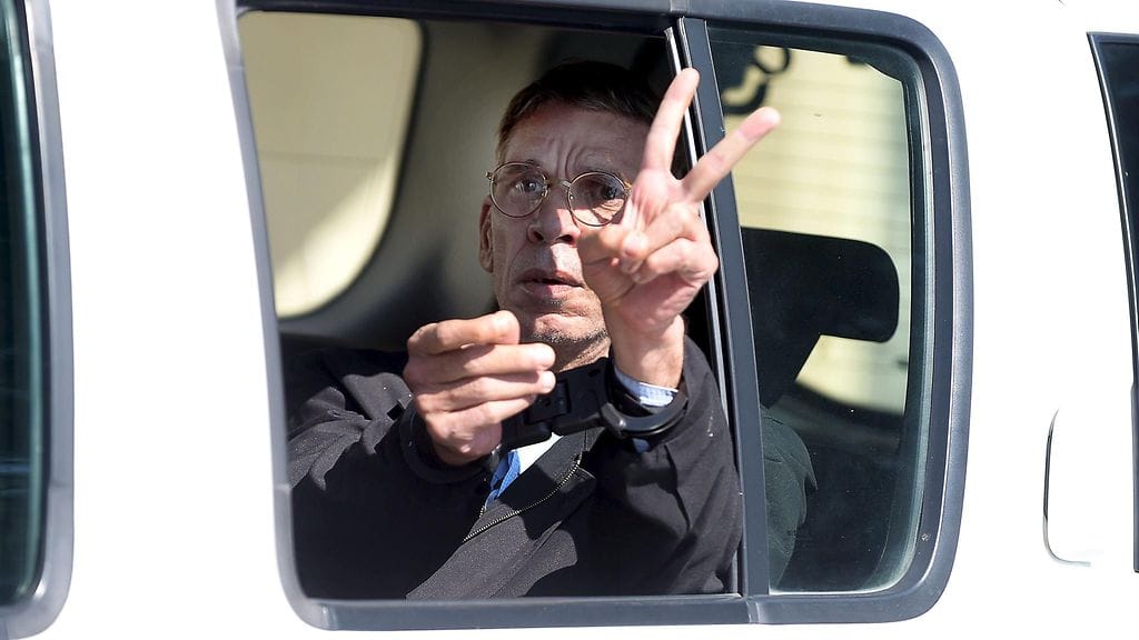 Mies näytti toimittajille voitonmerkkiä, kun hänet vietiin poliisiautoon.