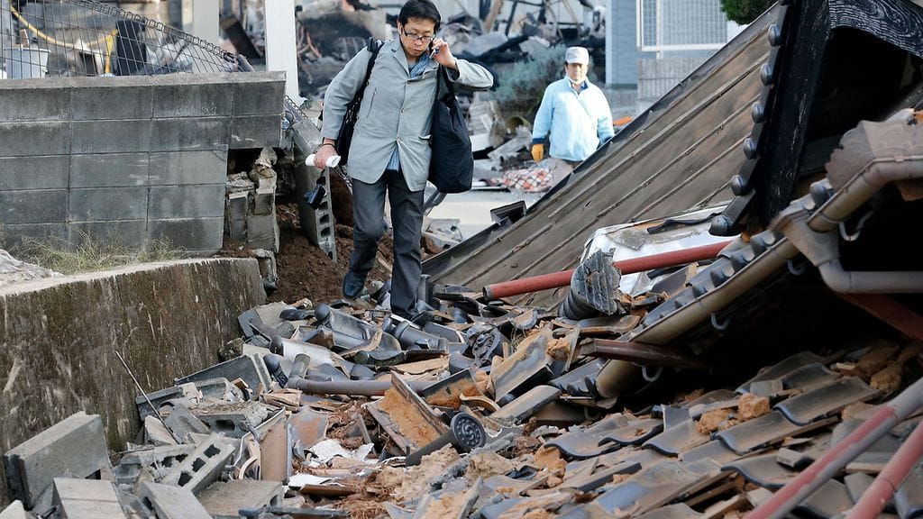 Mies kävelee talon raunioiden ohitse Mashikissa Kumamoton alueella Kyushun saarella Japanissa 16.4.2016. Alueelle on iskenyt lukuisia järistyksiä lyhyessä ajassa.