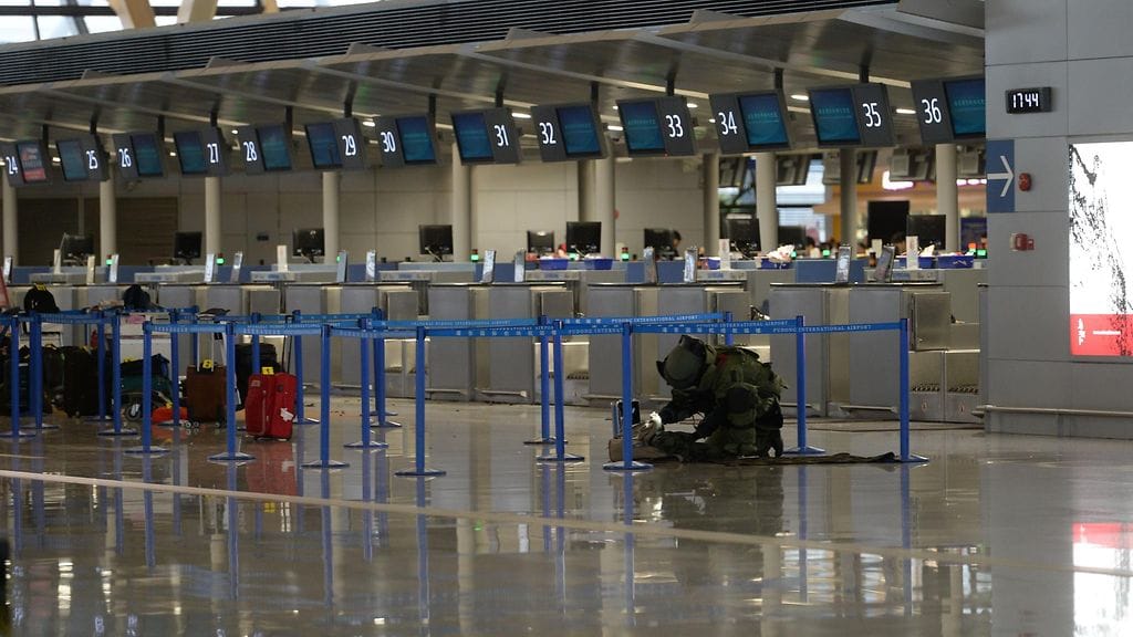 Mies salakuljetti kentälle repussaan lasipulloja, joiden sisälle hän oli piilottanut räjähteitä. Tämän jälkeen hän heitti yhden niistä lähtöselvitystiskiä kohti.