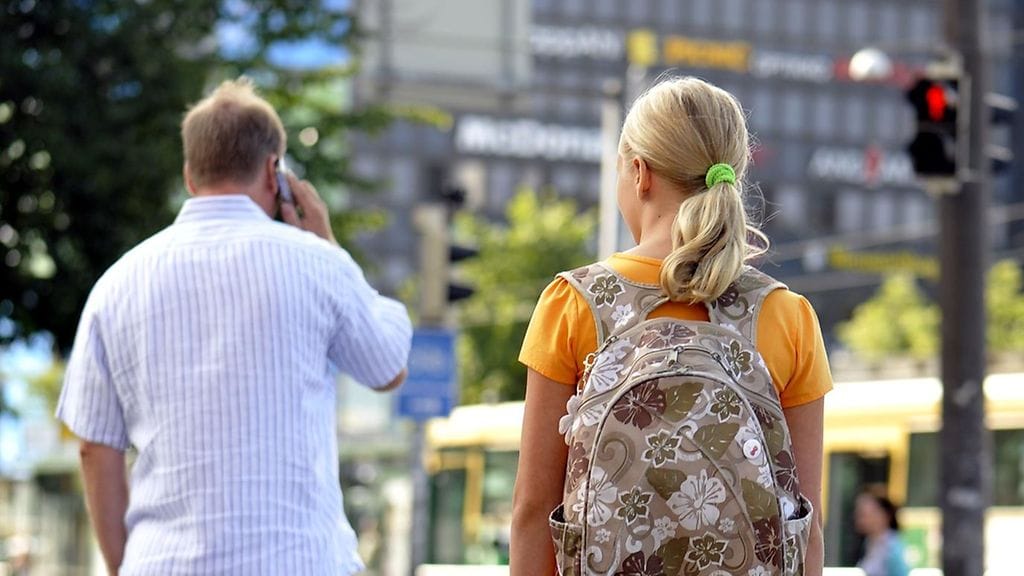 Lapsi odottaa valojen vaihtumista. Aikuinen kävelee päin punaisia.