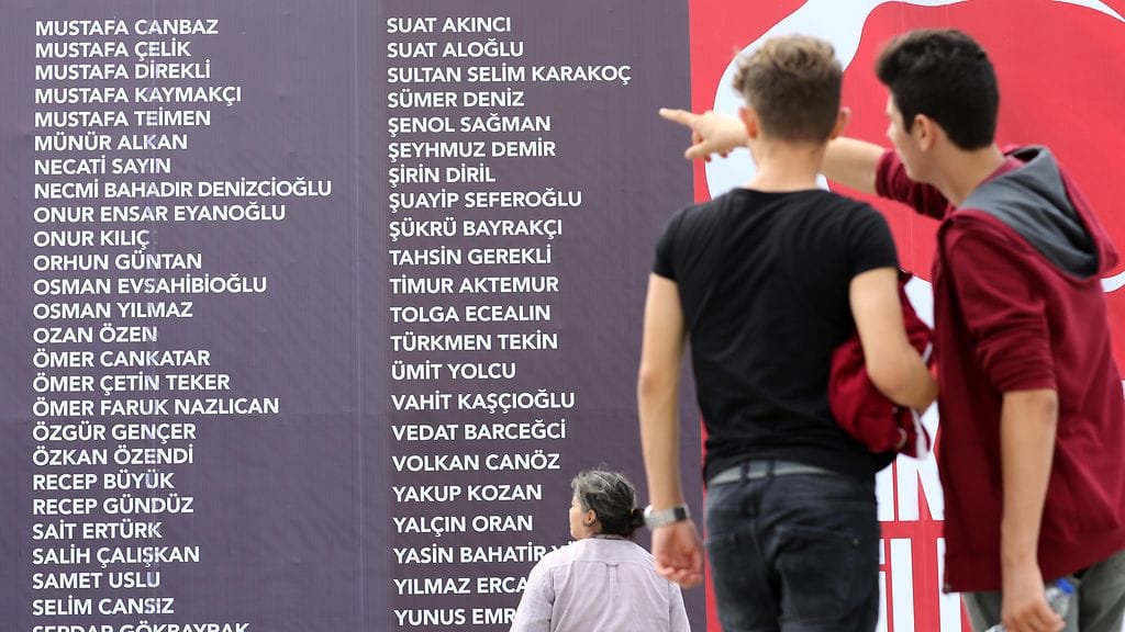 Ihmiset katsovat suurta seinää, johon on kirjoitettu 15. päivän vallankaappausyrityksessä kuolleiden nimet. Turkki on sittemmin siirtänyt jo 45 000 ihmistä työtehtävistään.