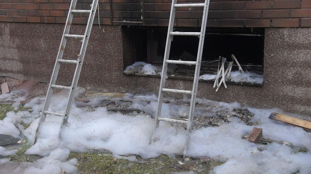 Heitetty palava esine sytytti omakotitalon kellarin tuleen, ja liekit levisivät ikkunan kautta tiilirakenteisen talon tuulensuojapapereista kattorakenteisiin. Maassa sammutusvaahtoa.