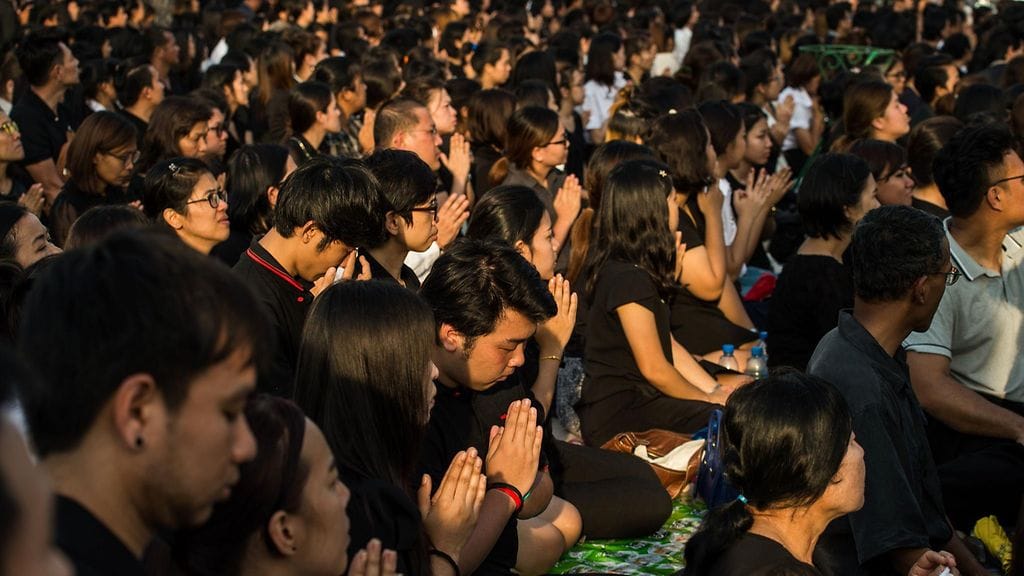 Tuhannet kaupunkilaiset ovat kokoontuneet Bangkokin kaduille seuraamaan ruumiin siirtoa.