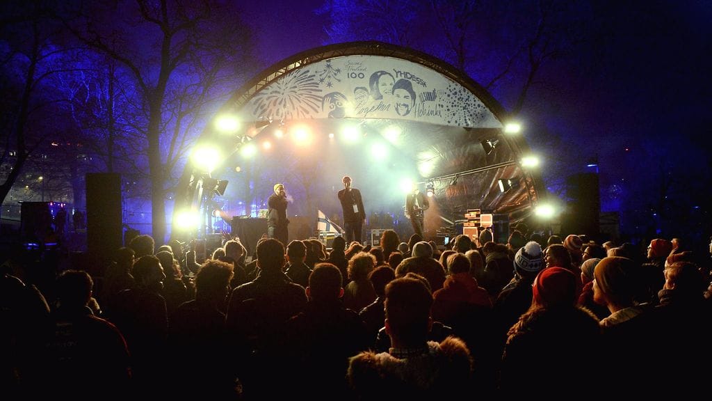 Yleisöä seuraamassa Puistolavalla Oopperan ja Finlandia-talon puolivälissä tapahtumaa Suomi 100 -juhlavuoden avajaisissa Helsingin Töölönlahdella.