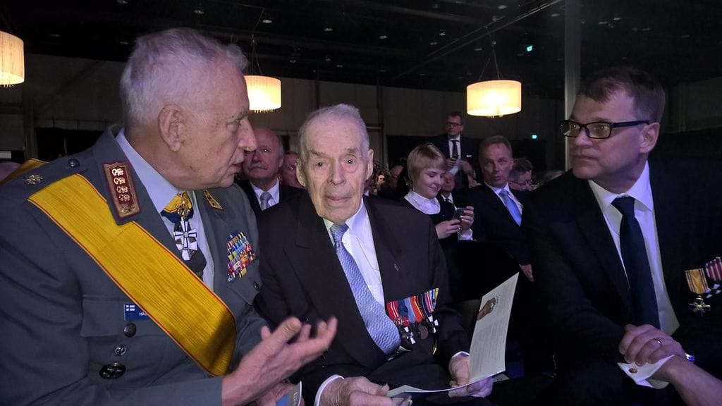 Sotaveteraani Sakari Sippola istuu kenraali Gustav Hägglundin ja pääministeri Juha Sipilän välissä Lahden veteraanijuhlassa.