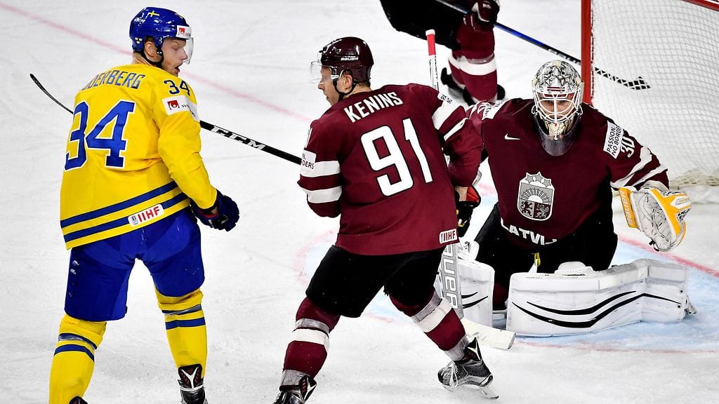Latvian hyökkääjä Ronalds Kenins vartioi Ruotsin Carl Söderbergiä maalin edustalla. Taustalla Latvian maalivahti Elvis Merzlikins.