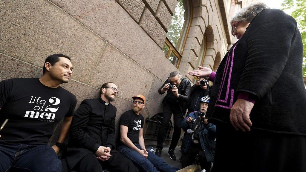 Piispa Irja Askola kävi tervehtimässä, kun pastori Kai Sadinmaa (kesk.) istuu vihkimänsä miesparin Raul Medinan (vas.) ja Hannu Virtasen (oik.) kanssa mielenosoituksellisesti jalkapuussa Helsingin hiippakunnan tuomiokapitulin edustalla Helsingissä.