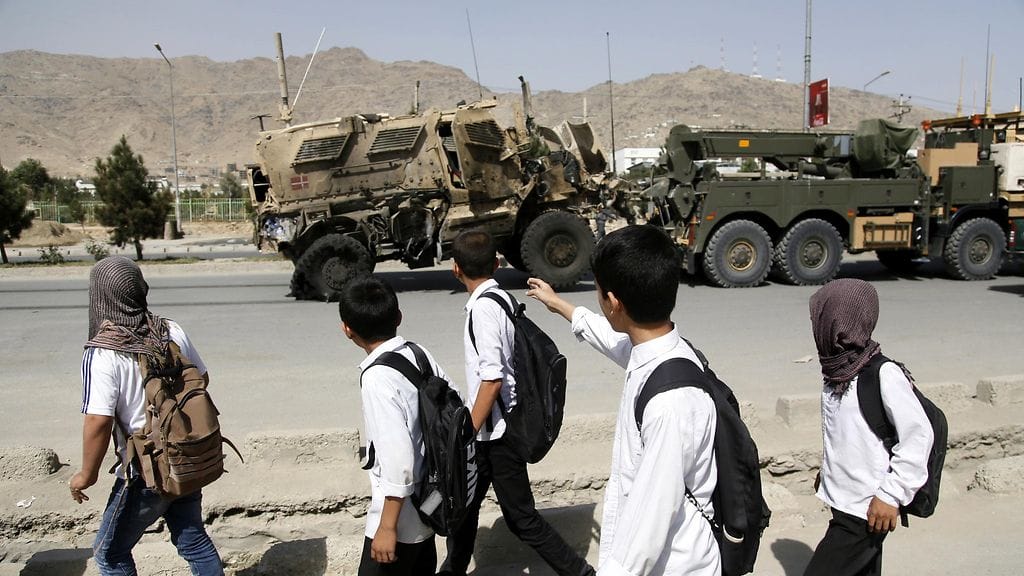 Koululaiset ohittamassa Tanskan joukkojen romuttunutta autoa Kabulissa.