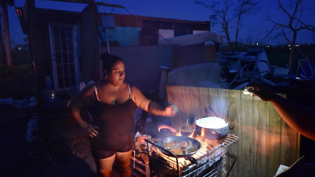 Nainen valmistaa ruokaa tuhoutuneen kotinsa edustalla.