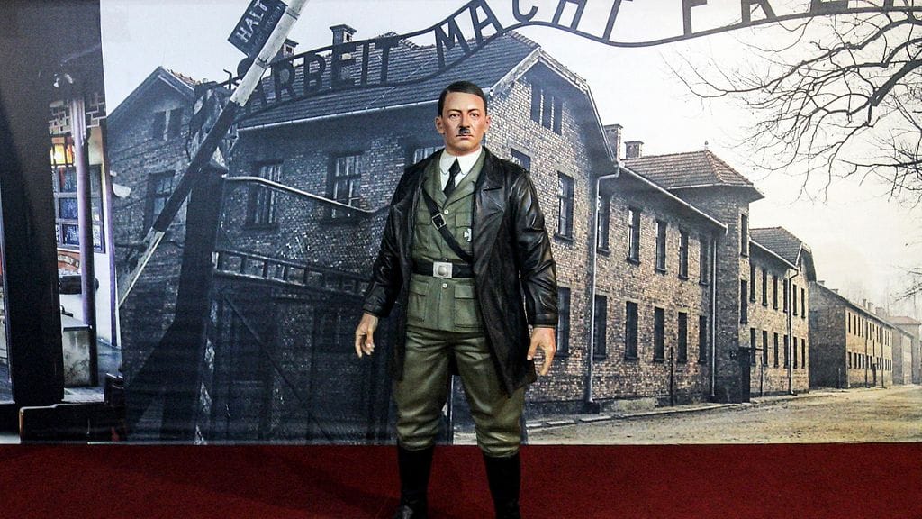 Aidon kokoisen vahapatsaan taustalla on Auschwitzin keskitysleiri.