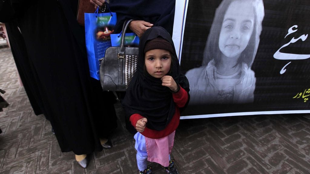 Pieni tyttö seisoo kuolleena löydetyn Zainabin kuvan edessä Pakistanissa.