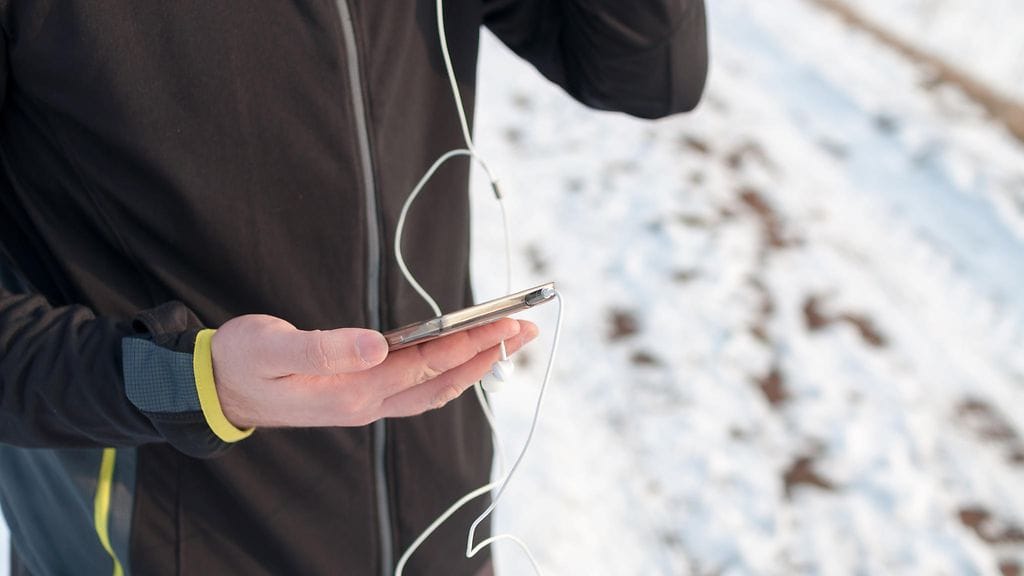 lenkkeilijä kännykän ja kuulokkeiden kanssa talvella