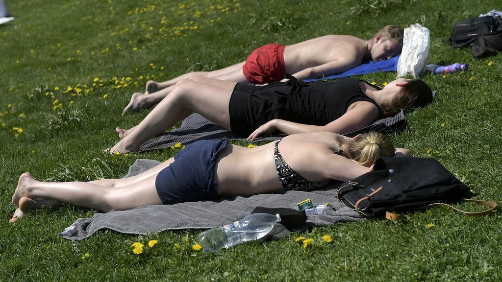 Auringonpalvojat nauttivat helteistä Merisataman nurmikolla Helsingissä.