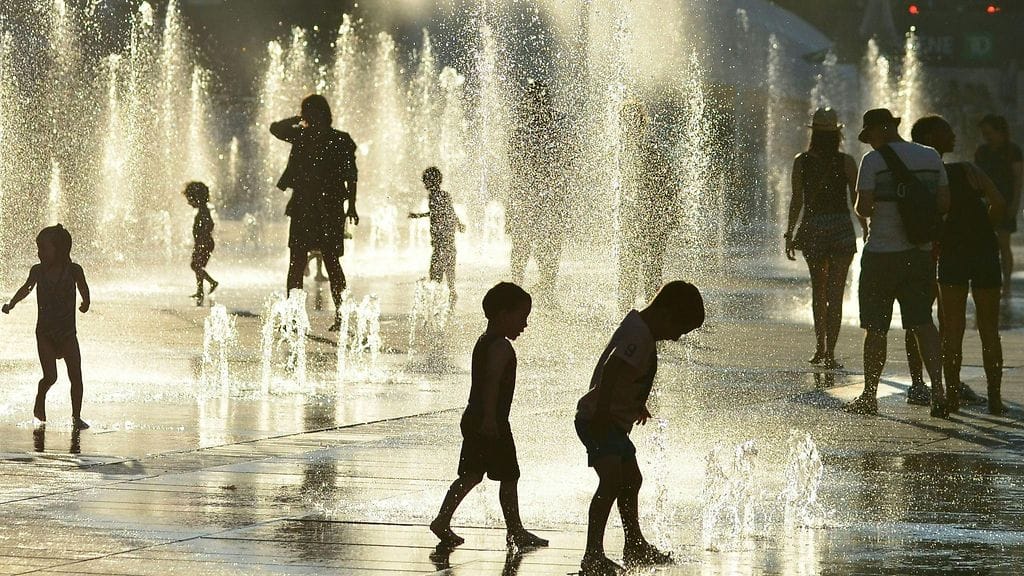 Ihmiset viilentävät itseään suihkulähteiden luona hellepäivänä 3.7.