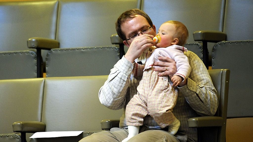 Äitiyden ihanne on tutkijan mukaan yhä tiukempi kuin isyyden. Kuvituskuvassa isä ja lapsi eduskunnan lehtereillä.