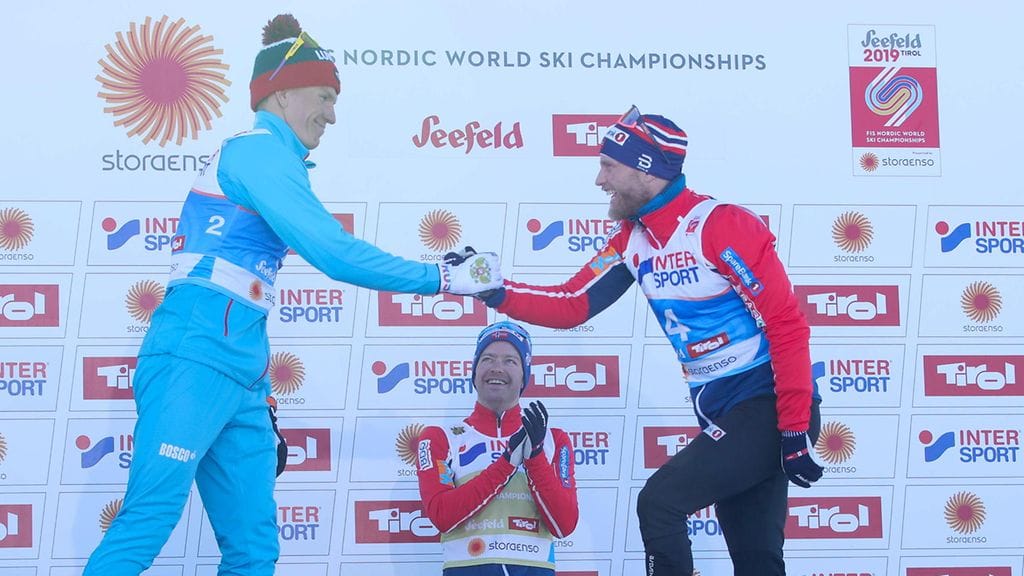 Aleksandr Bolshunov (vas.) ja Martin Johnsrud Sundby kättelivät yhdistelmäkisan jälkeen palkintopallille. Takana taputtaa mestari Sjur Röthe.