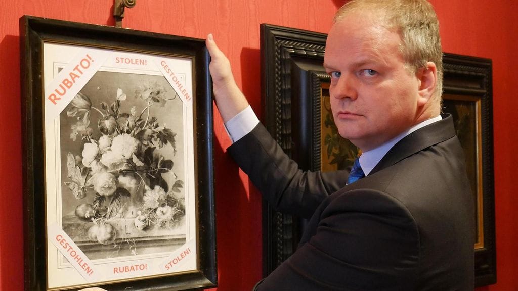 Uffizin Gallerian johtaja Eika Schmidt pitää käsissään mustavalkoista kopiota taulusta, jossa kerrotaan, että alkupräinen teos on varastettu.