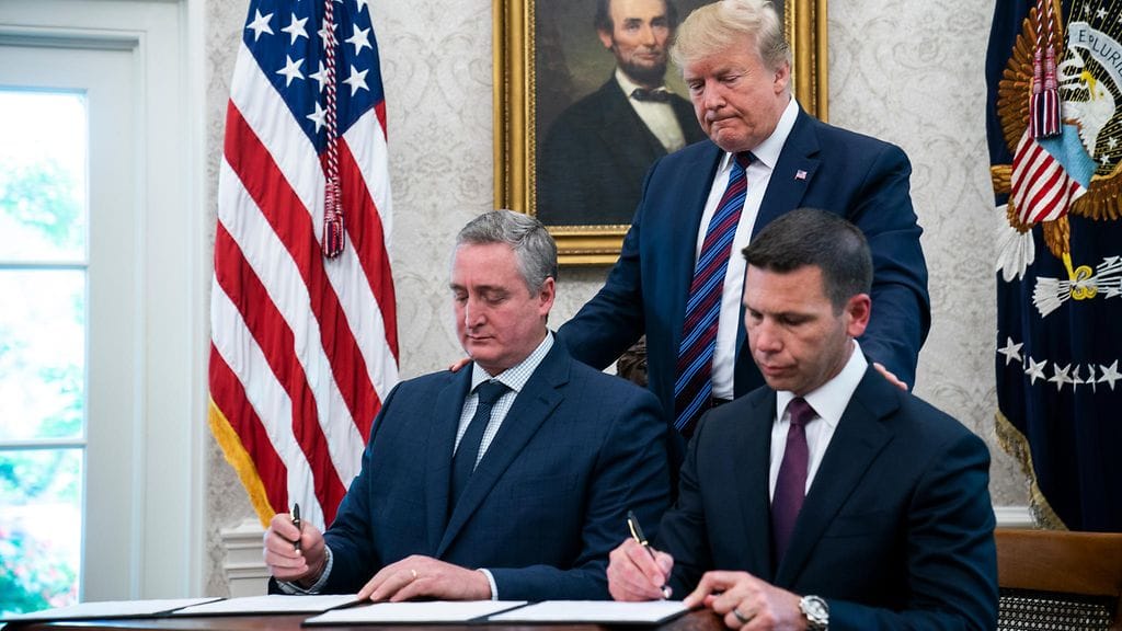 Presidentti Donald Trump seuraa taustalla, kun kansallisen turvallisuuden ministeriön sihteeri Kevin McAleenan (oik.) ja Guatemalan sisäministeri Enrique Degenhart (vas.) allekirjoittavat sopimusta.