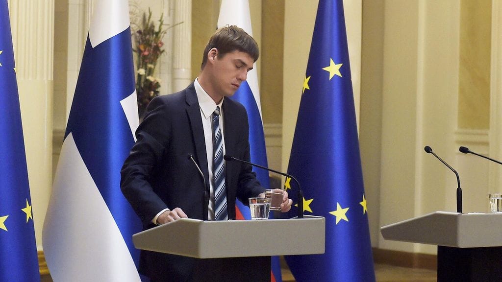 Tummaan pukuun sonnustautunut mies vaihtaa Vladimir Putinille asetetun juomalasin.