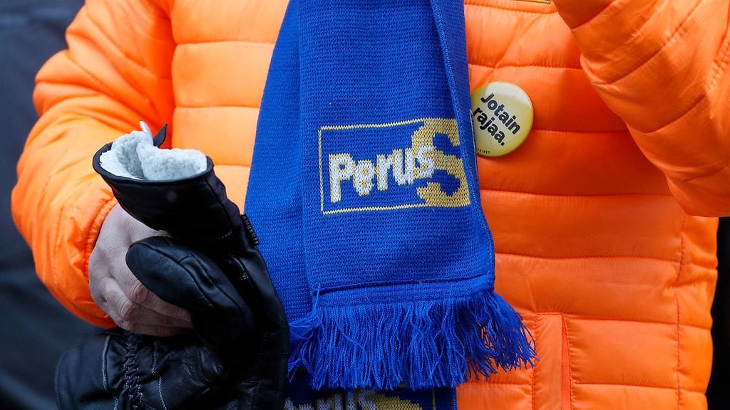 Perussuomalaisten logo ja iskulause henkilön vaatteissa puolueen vaalitilaisuudesta Joensuussa maaliskuussa.