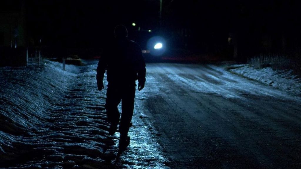 Jalankulkija pimeällä tien laidassa. Kuvituskuva.