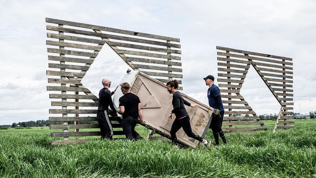Päällikkö-kilpailijat joutuvat kantamaan täynnä olevaa bajamajaa.