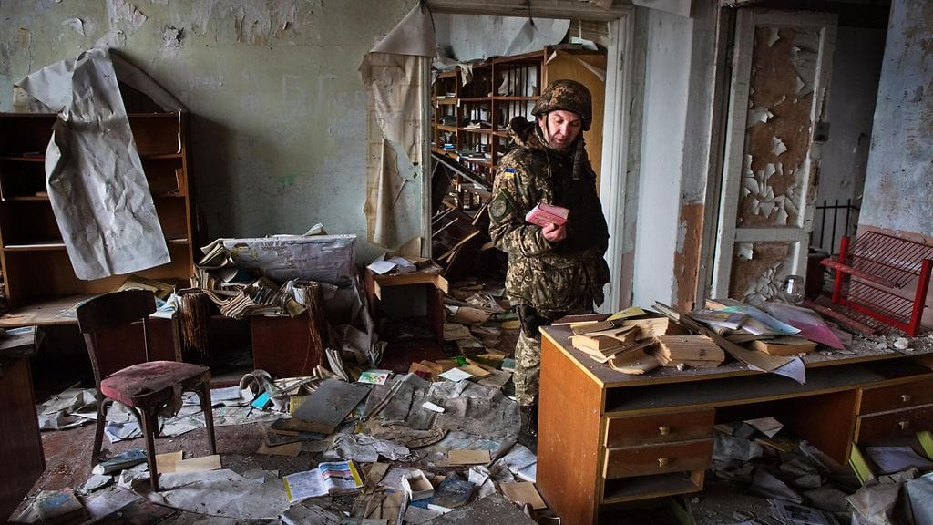Ukrainan sotilas tutki koulurakennuksen tavaroita konfliktissa tuhoutuneessa Piskyn kylässä, Itä-Ukrainassa vuonna 2017.