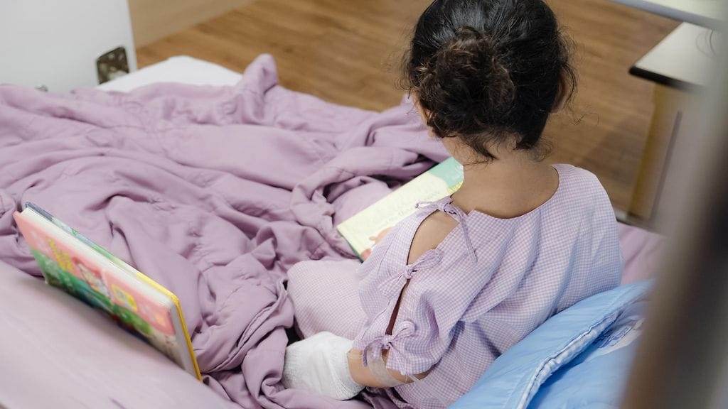 Dane käyttää teho-osastolla verenhapetuslaitteita, joiden ansiosta potilaan sydän ja keuhkot saavat levätä ja toipua. Häneltä löytyy silti aikaa istua lasten vierellä kirjan kanssa. Kuvituskuva.