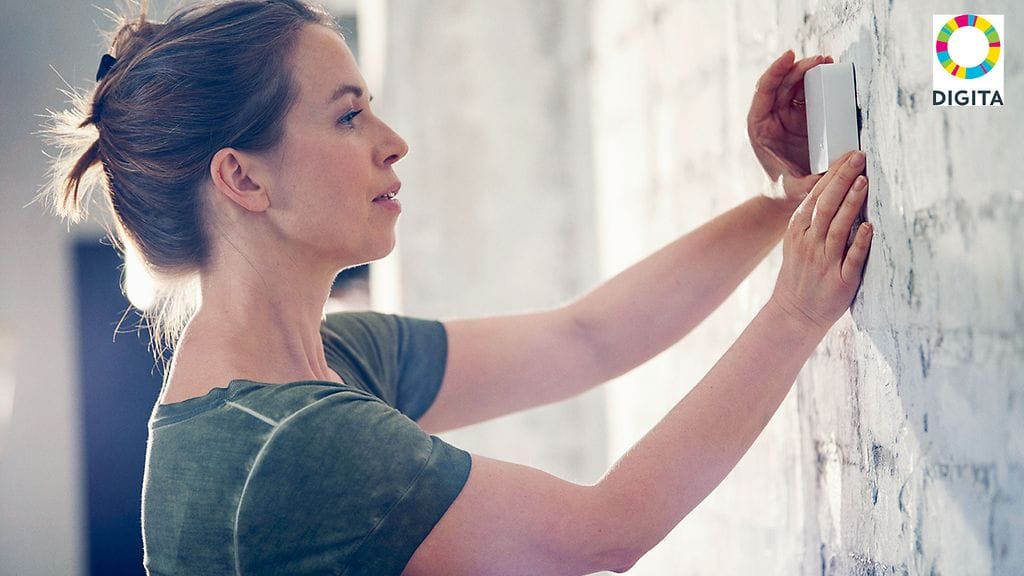 Kuvassa nainen laittaa olosuhdeanturia kotinsa seinälle.